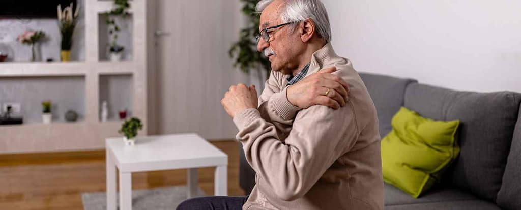 Longevità, patologie e dolore cronico
Un signore anziano seduto sul suo divano di casa si tocca la spalla dolorante.