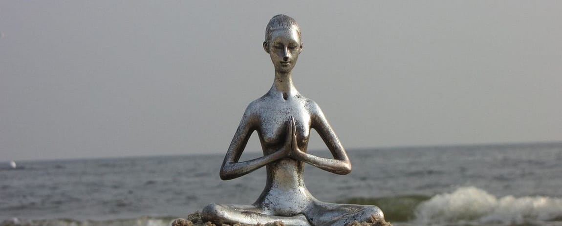 una statuetta a forma di una donna filiforme in metallo che medita sulla spiaggia