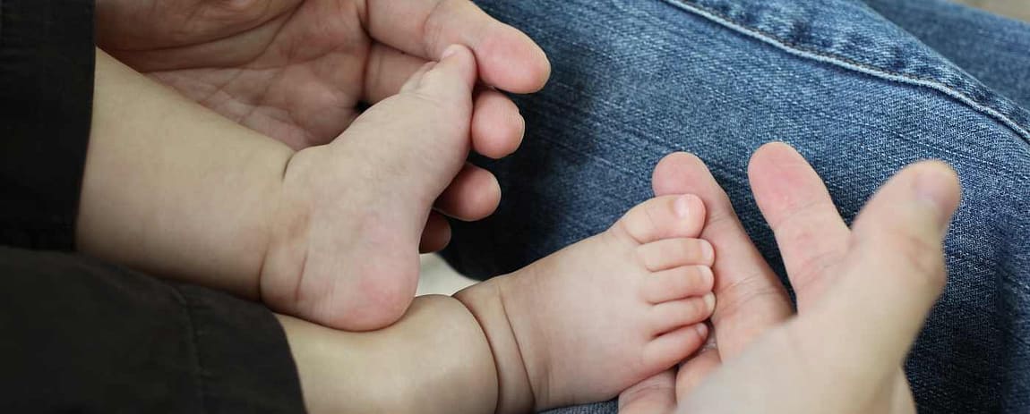 Due mani adulte di un genitore, tengono su di loro i piedini di un bambino piccolo.