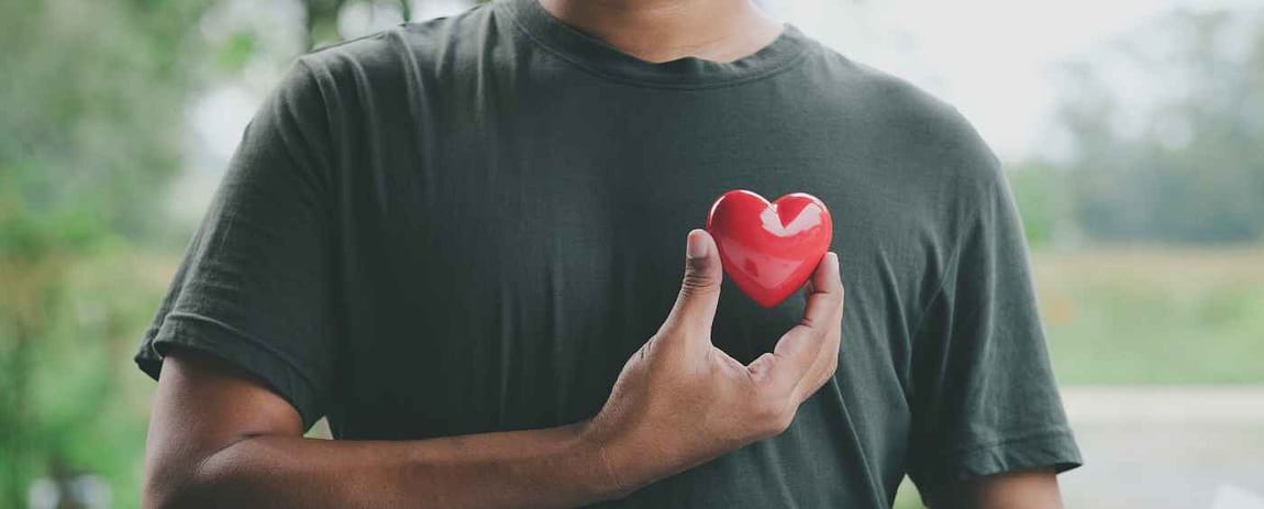 Un uomo avvicina davanti al petto un cuore rosso. Con la maglietta grigia, il colore fa un bellissimo contrasto.