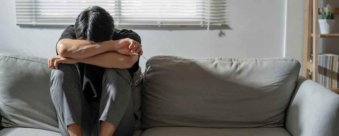 Un uomo su di un divano in un atteggiamento di forte chiusura manifesta il suo enorme disagio.
