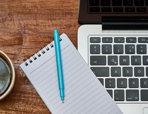 Un computer moderno, aperto con affianco un tacquino e una tazza di caffè