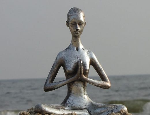 una statuetta a forma di una donna filiforme in metallo che medita sulla spiaggia