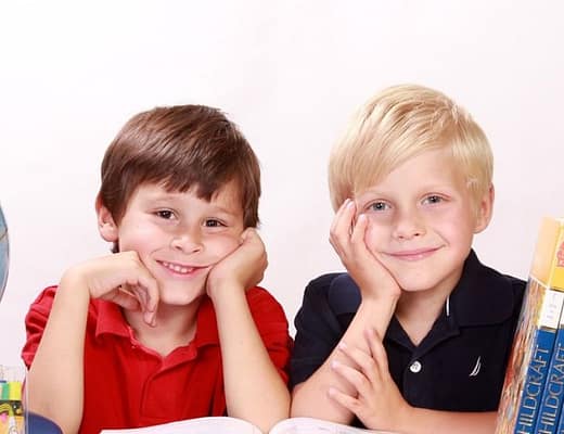 Due ragazzini sono in posa, sorridendo, tra un mappamondo e dei libri di scuola.