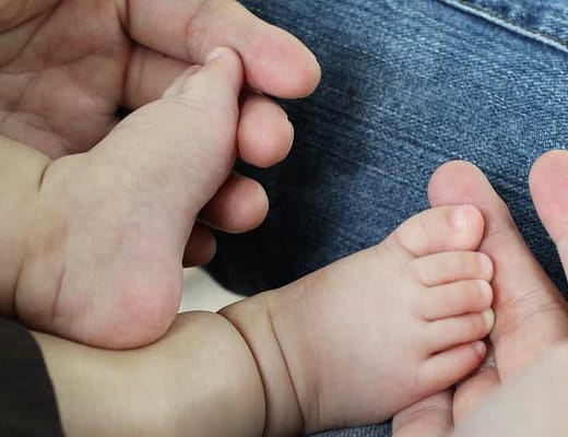 Due mani adulte di un genitore, tengono su di loro i piedini di un bambino piccolo.