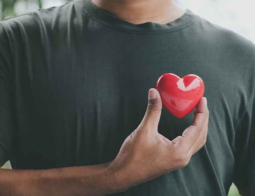 Un uomo avvicina davanti al petto un cuore rosso. Con la maglietta grigia, il colore fa un bellissimo contrasto.
