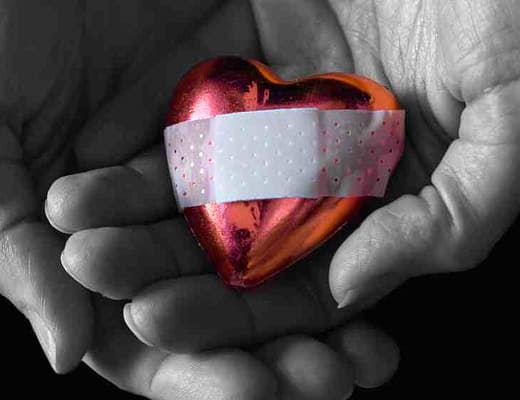 Un cuore con un cerotto è custodito tra le mani di una persona in bianco e nero.