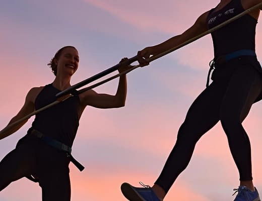 Due funamboli che camminano su due rette diverse, parallele con una barra equilibratrice condivisa.