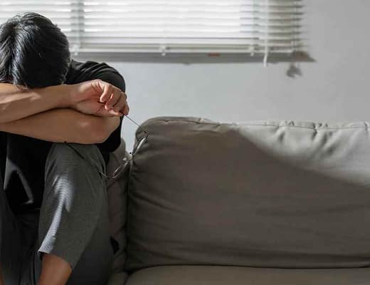 Un uomo su di un divano in un atteggiamento di forte chiusura manifesta il suo enorme disagio.